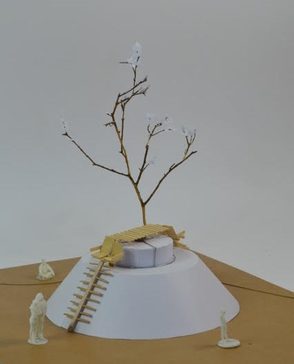 photographie en plongée d'une maquette miniature d'une strucure en bois posée sur un puit en papier avec un arbre.