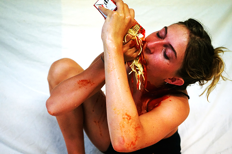 photographie saturée d'une fille accroupie en train de manger des spaghettis à la main.